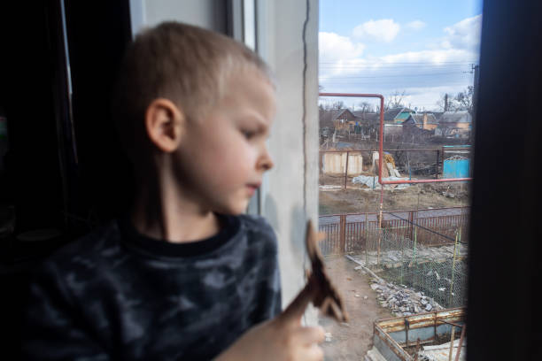 niño sentado en la ventana y sosteniendo un avión de combate de juguete - ukraine war fotografías e imágenes de stock