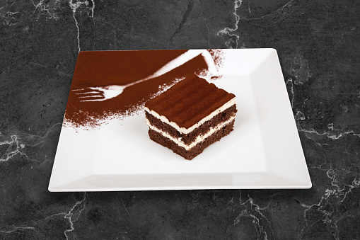Tiramisu, chocolate bars with milk mousse. It is served on a white plate on a black background.