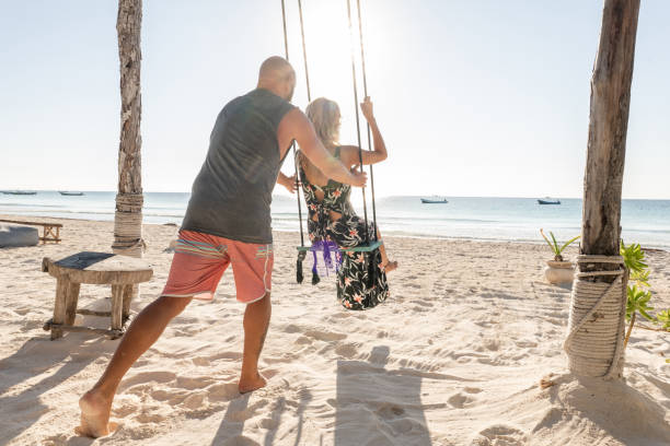istock Couple on the beach at sunrise playing on swing 1381315812