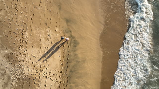Aerial view of couple walking along empty beach, at sunrise