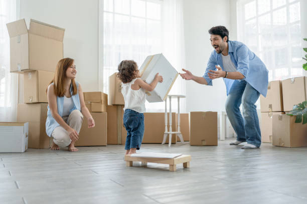 Little girl carrying box to her father while they packing boxes for moving to new house. Father and mother have happy looking their daughter stock photo