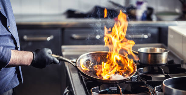 chef sosteniendo una sartén que realiza flambe en un plato en ella. - hot dish fotografías e imágenes de stock
