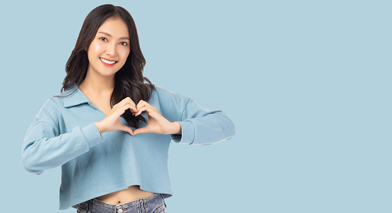 Smiling young girl showing heart with two hands, love sign Isolated over light blue background Portrait young beautiful asian woman hand gesturing in heart shape Smile face asian girl get in love
