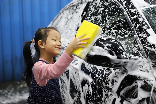 Asian girls learning how to wash a car for their father.