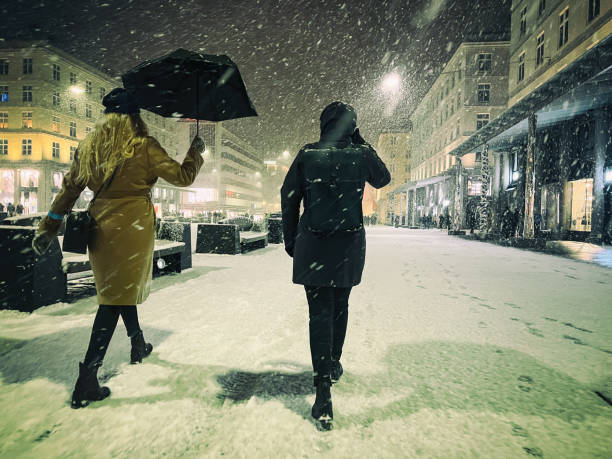 Snow storm over the city during a winter night, while city life proceeds as normal. Two women walk in the city street resisting to the heavy snow storm
