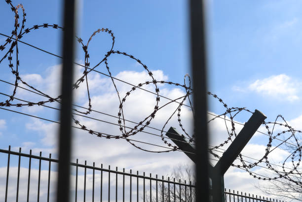 istock Barbed wire against a cloudy sky on a big fence at a border. 1381407644