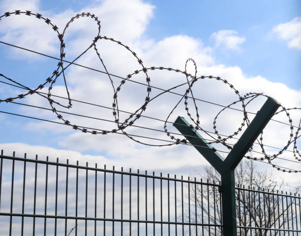 istock Barbed wire against a cloudy sky on a big fence at a border. 1381407661