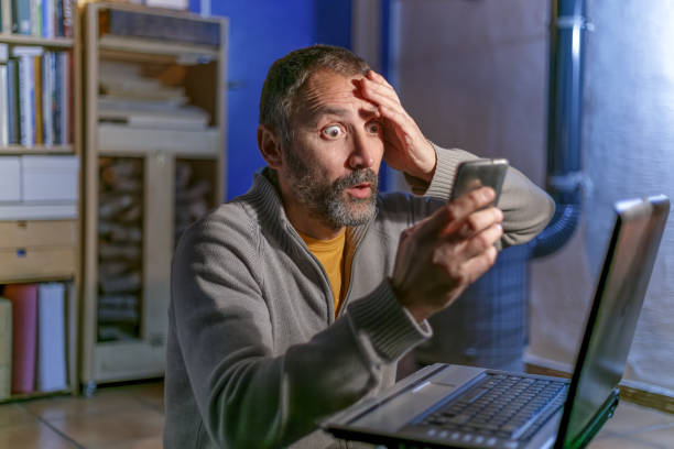 Incredulity gesture in middle-aged man looking at his cell phone next to laptop. Rustic home interior with wood burning stove and stacked firewood Madrid, Spain. January 19 2022. Incredulity gesture in middle-aged man looking at his cell phone next to laptop. Rustic home interior with wood burning stove and stacked firewood confusion raised eyebrows human face men stock pictures, royalty-free photos & images