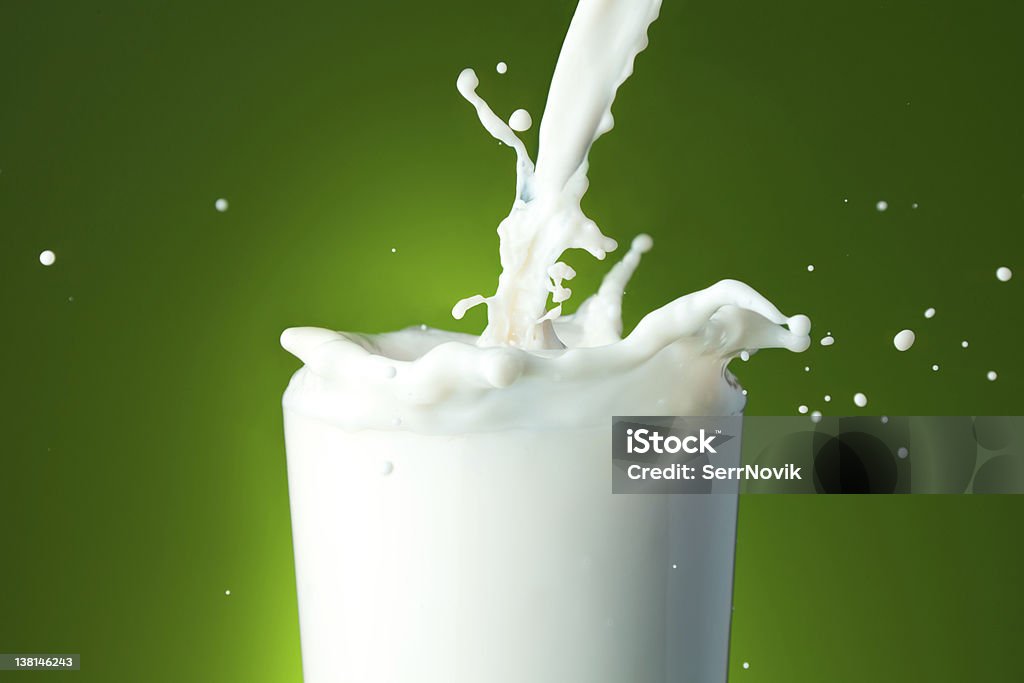 Filling the glass with milk Close-up of a glass with milk that splashing on green background Clean Stock Photo