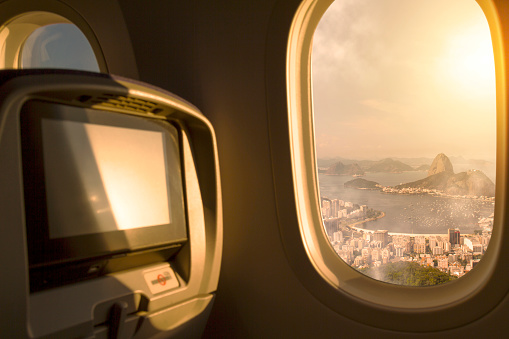 Rio de Janeiro City, Brazil sunset / sunrise sky aerial view from porthole window airplane economic seat after take off from airport. On back, Guanabara Bay, Sugar Loaf and Botafogo Beach. Travel concept. Plane interior.