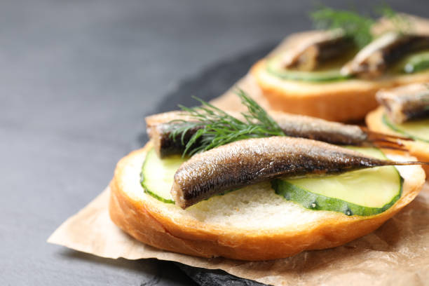 istock Delicious sandwich with sprats, cucumbers and dill on slate board, closeup 1381486015