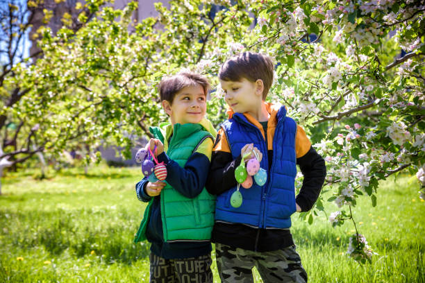 Two sibling brothers friends after successful egg hunt standing and smiling with Easter eggs in their hands. Traditional Easter hunt outdoors.