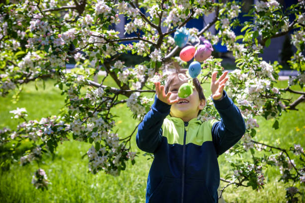istock Boy throwing up color Easter Eggs after egg hunt. Traditional Easter concept. Happy boy smiling on green blooming field background 1381490527