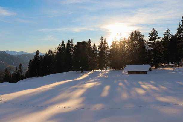 The last sunlight throws shadows in the snow next to a small hut