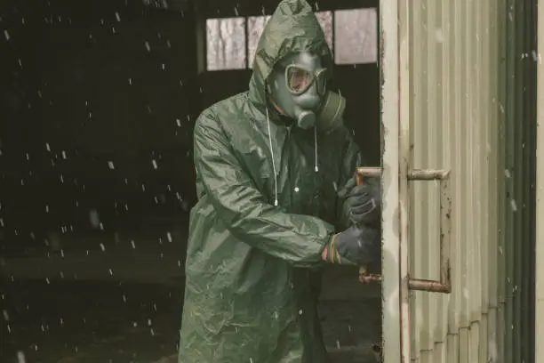 Adult man wearing protective gas mask and clothes taking shelter at some ruined building. Actor performance.