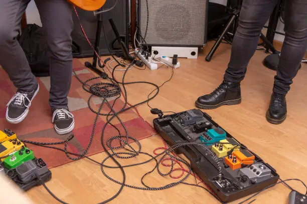 GUITARIST'S PEDALS ON THE FLOOR SURROUNDED BY CABLES