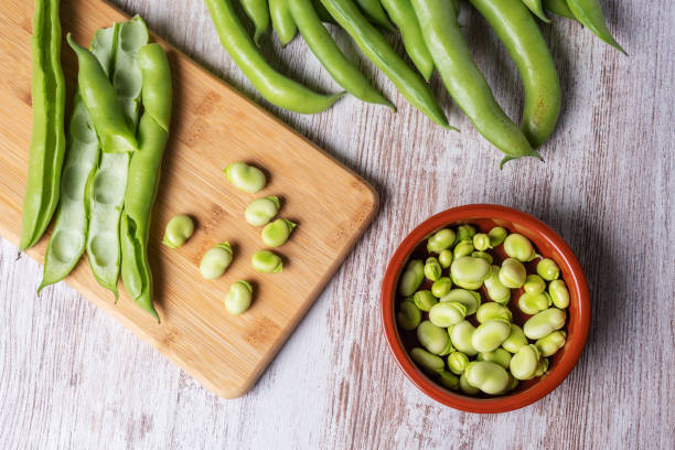 saubohnen auf einem weißen holztisch, draufsicht. - fava bean stock-fotos und bilder