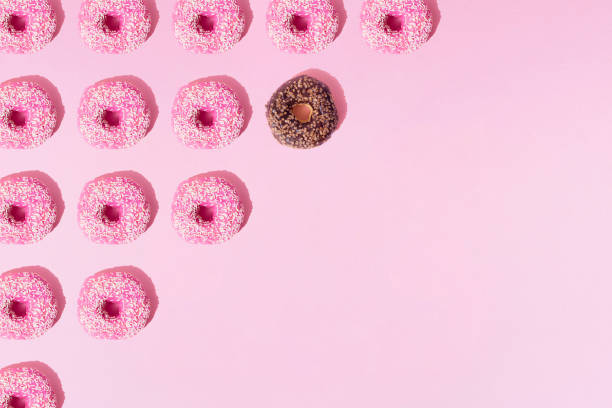 istock Arranged ring donuts like triangle with chocolate and pink glaze. Small crumbs on a pink pastel background. Minimal design. Pattern and copy space. 1381564973
