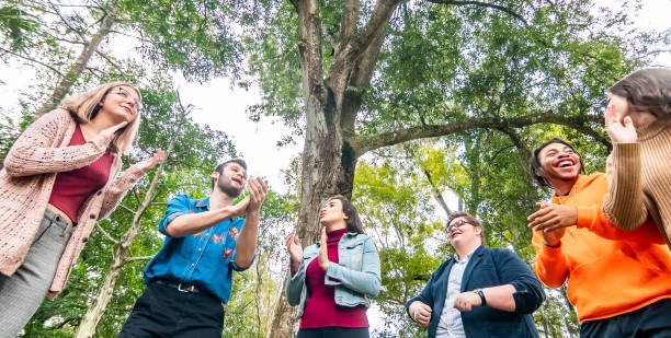 grupo diverso y feliz de jóvenes que se ríen aplaudiendo y cantando al aire libre, grupo juvenil o club o tal vez formación de equipos - cántico fotografías e imágenes de stock