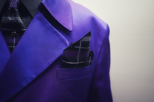 A close up of a man in a purple suit against a white background