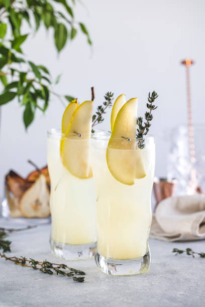Pear Collins Cocktail. Two highball glasses filled with pear puree cocktail or mocktails surrounded by ingredients and bar tools stock photo
