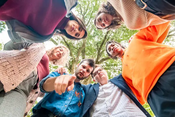 Photo of Group of people, mixed race and gender university students in a circle with arms around each other  looking at camera,  judgmental and shame