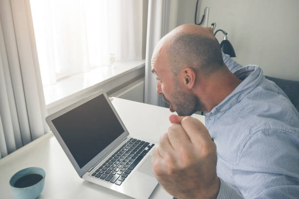 Well dressed overly happy male looking joyful and surprised at his laptop in minimalistic scandinavian apartment.