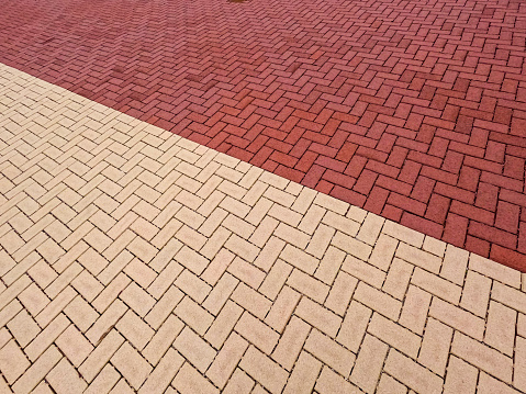 Diagonal split between creme colored brick and red brick outdoor surface. Contrasting brick colors in a herringbone layout pattern.
