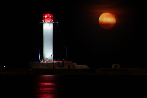 Vorontsov Lighthouse night against the rising of the big red moon. Old white beacon lantern lighthouse in the Black Sea port of Odessa, Ukraine. Long exposure.