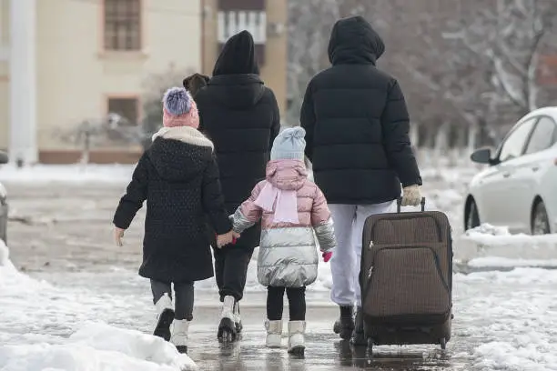 a family of four with a dog leaves the city for a trip and walks along the road with a large suitcase in the winter season through the snow