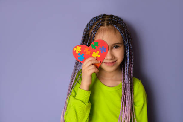 A girl holds a heart with puzzle pieces in her hands A girl with blue-purple Afro pigtails in a light green top holds a heart with puzzle pieces in her hands as a sign of solidarity with people suffering from autism spectrum disorder. World Autism day autism stock pictures, royalty-free photos & images