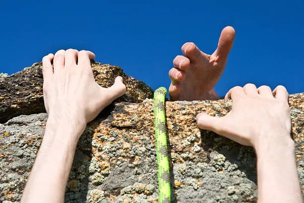 Hands of climber on brink of rock needing the help