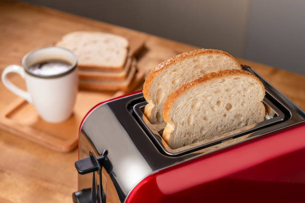 On the kitchen table is a red toaster and a cup of coffee.