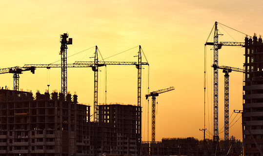 Construction site with frames of multistory buildings and cranes at evening yellow sunlight sky