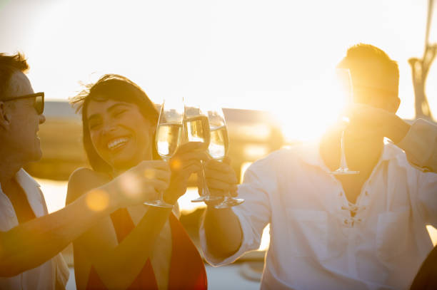 un gruppo di amici uomini e donne caucasici si divertono a bere champagne mentre il catamarano naviga in vacanza estiva - drink alcohol summer celebration foto e immagini stock