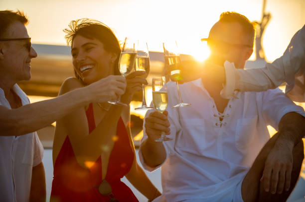 grupa kaukaskich przyjaciół mężczyzn i kobiet lubi pić szampana podczas rejsu katamaranem na letnie wakacje - sunset yacht luxury sailboat zdjęcia i obrazy z banku zdjęć