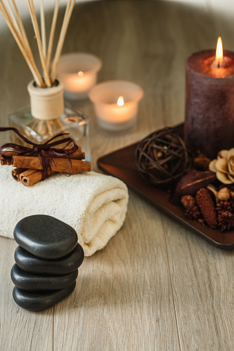 Tranquil scene if black stones for lastone therapy stacked in a row, incense, candles and towel decorated with cinnamon sticks.