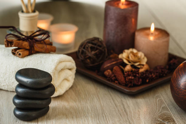 Selective focus of multiple candles lit, decorative flowers, incense, towels, cinnamon sticks and black stones for lastone therapy arranged for a more pleasant atmosphere.