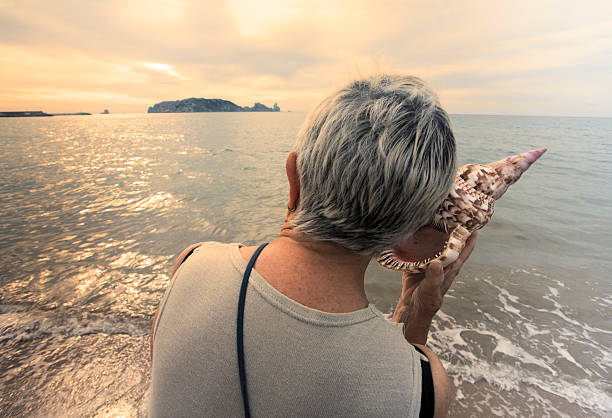World speak, I´m listening Woman with conch next to sea Woman listening  to the sound of the inside of a conch next to the beach at dusk. conch shell photos stock pictures, royalty-free photos & images
