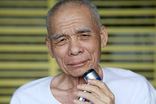 An Asian senior man is shaving his moustache at home.
