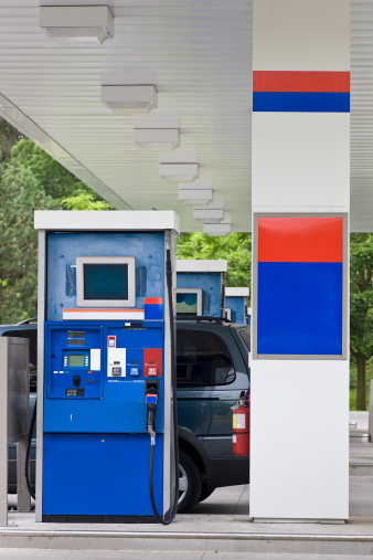 A gas station highlighting a gas pump and a portion of a minivan stopping to fill up.