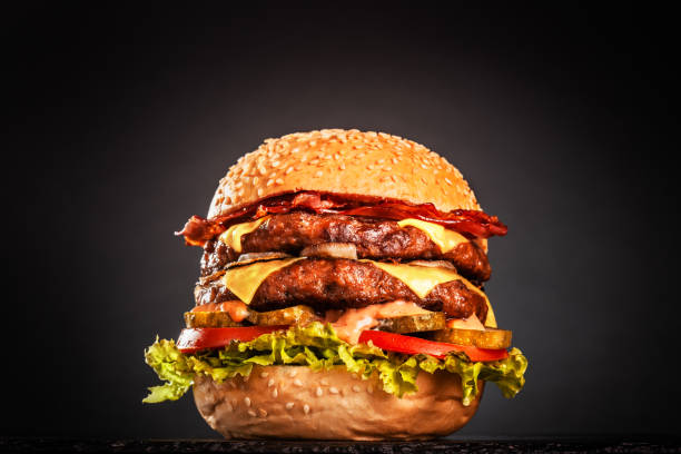 istock Double burger with bacon cheese onions tomatoes cucumber and lettuce. Isolated on black background.. 1381881764