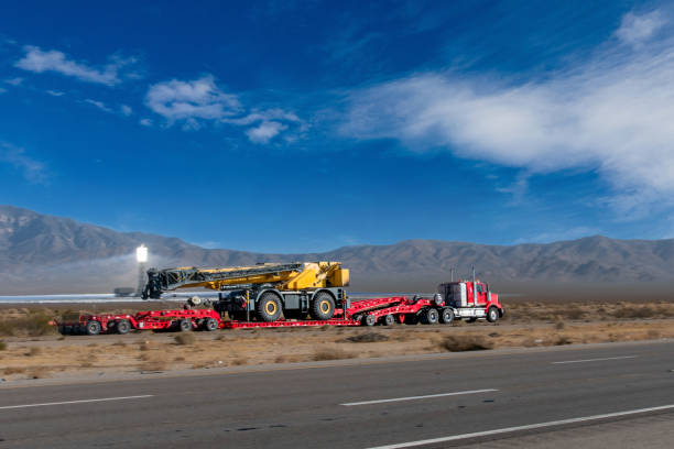 полугрузовик перевозит большой грунтовый двигатель на четырехполосном шоссе возле солнечной электростанции иванпа - vehicle trailer стоковые фото и изображения