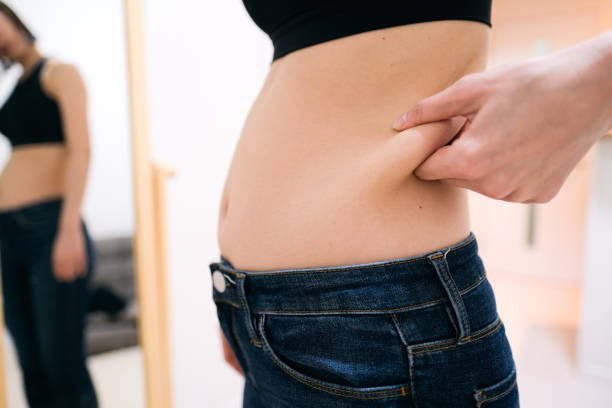 istock Young woman looking at stomach fat by mirror 1381902094