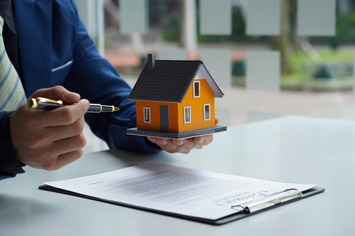 Sales representative. Holding a house, offering customers to sign a contract. Sign official documents. Customer partners buy or sell real estate. The sales representative offers a contract to purchase a house.