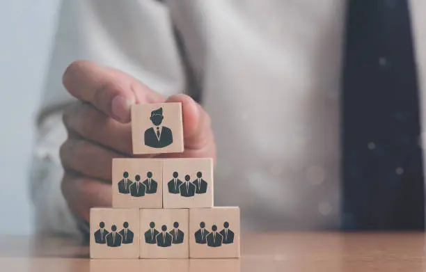 Photo of Hand putting wood cube block on top pyramid, Copy space. Resource management and recruitment business concept.