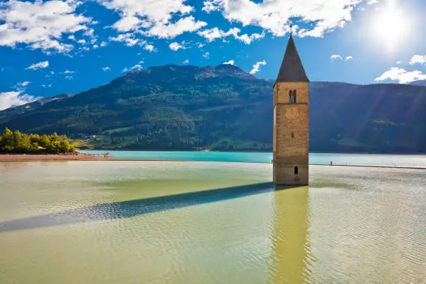 Submerged bell Tower of Curon Venosta or Graun im Vinschgau on Lake Reschen sun haze view, South Tyrol region Italy