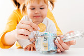 Baby girl and her mother puts bitcoin in a glass jar with currency. Close up. The concept of investing and online banking