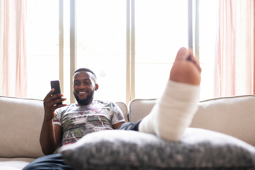 Man smiling with injured foot using phone to check insurance