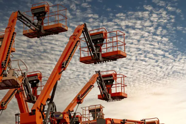 Photo of Articulated boom lift. Aerial platform lift. Telescopic boom lift against blue sky. Mobile construction crane for rent and sale. Maintenance and repair hydraulic boom lift service. Crane dealership.